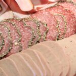 Immagine di diversi insaccati su un tagliere, evidenziando i salumi "magri" e il loro contenuto di colesterolo.